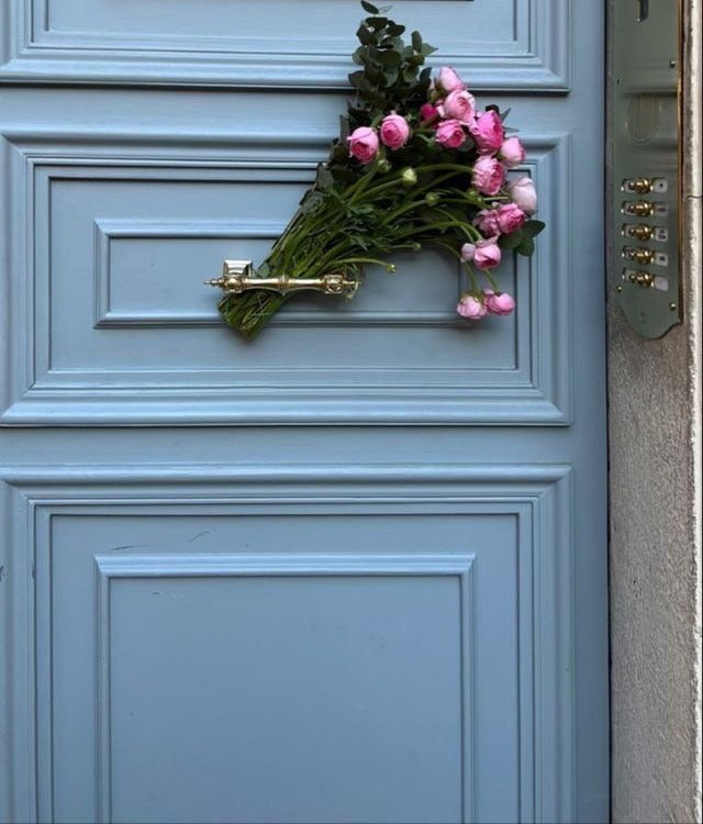A bunch of pink ranunculus tucked into the handle of a pale blue front door
