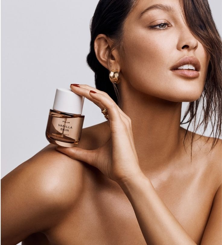 A woman holding a small glass fragrance bottle against her shoulder
