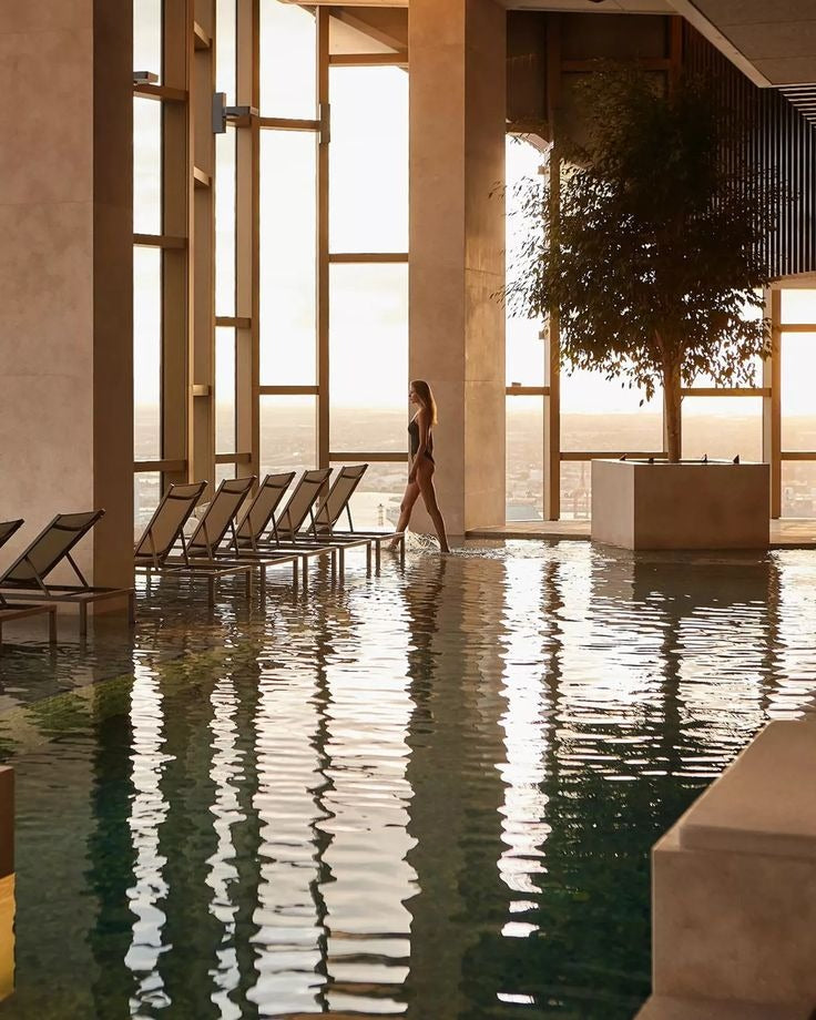 A figure walking beside an indoor pool lit through tall windows