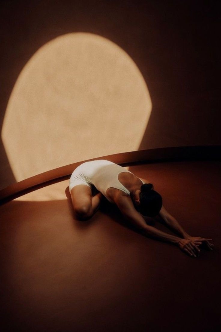 A disc of warm light on a wall above a figure stretching on the floor