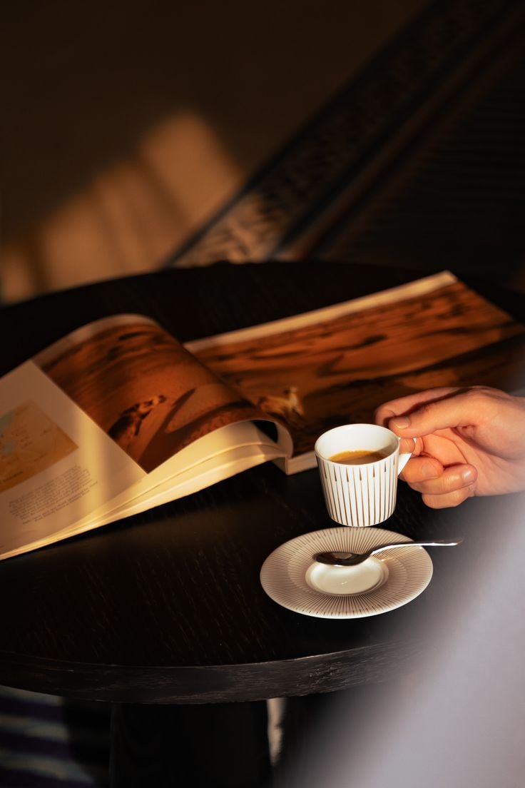 An open magazine beside an espresso cup on a dark café table